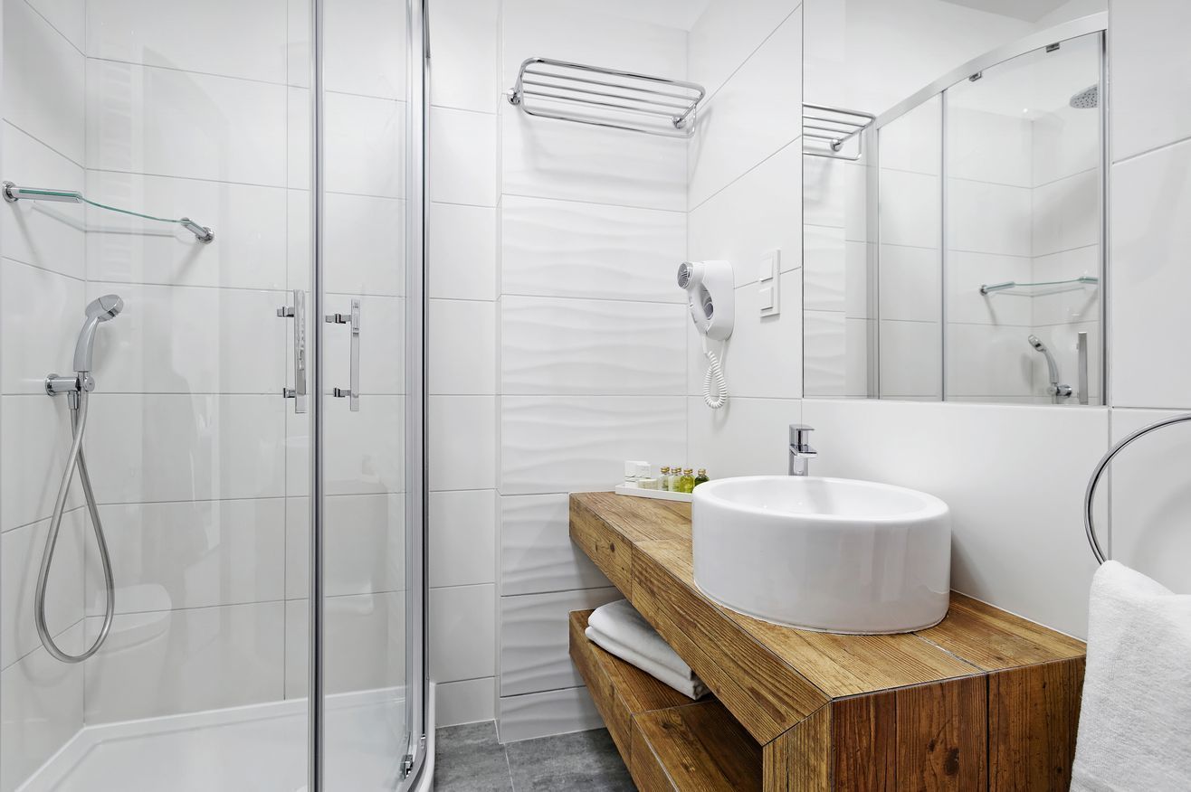 Un baño moderno con ducha de vidrio, tocador de madera y un lavabo blanco, además de un espejo grande.