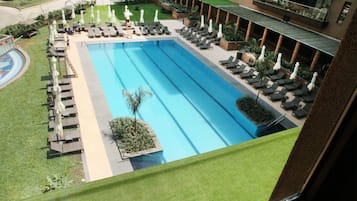A large rectangular pool with lounge chairs and umbrellas around it, surrounded by a well-maintained lawn and a building in the background.