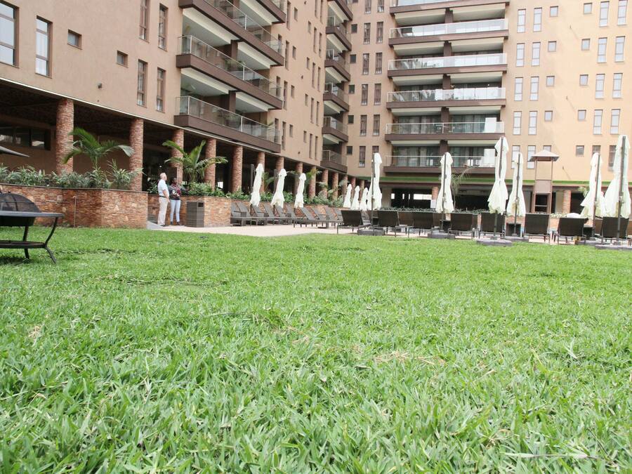 A grassy courtyard with outdoor seating and umbrellas, surrounded by a multi-story building with balconies.