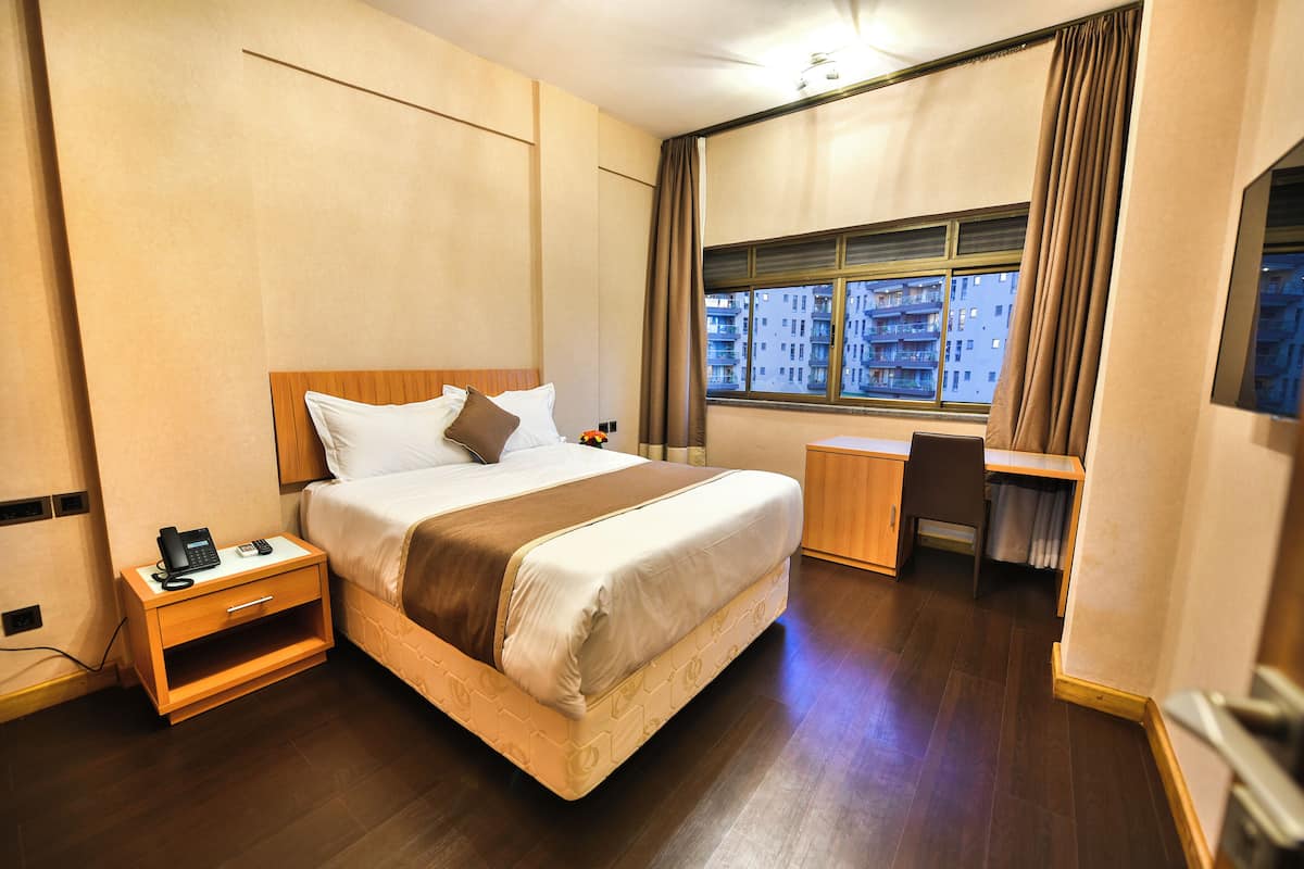 A hotel room with a bed, bedside table with a phone, a desk, and a chair.