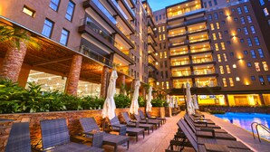 Un hotel con varios pisos, asientos al aire libre con sombrillas y una piscina.