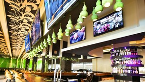 Zona de bar con varias pantallas, una barra y diferentes opciones de asientos.