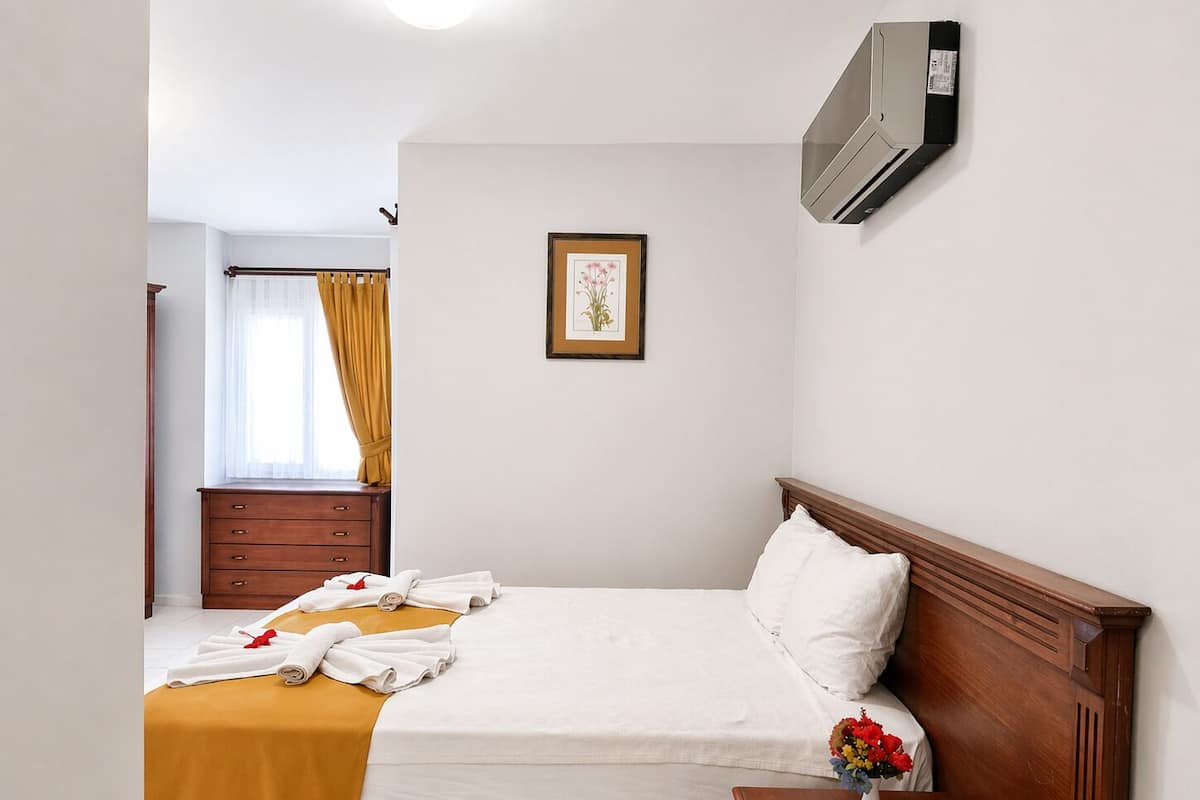 Una habitación de hotel con una cama, una mesita de noche de madera, un cuadro enmarco y una ventana con cortinas.