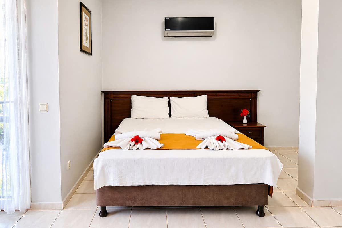 Habitación de hotel con cama, mesita de noche, aire acondicionado montado en la pared y ventana con cortinas.