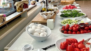 A buffet table with various food items, a window with a view of greenery, and a wall with a flag and a mounted lamp. - Villa Anfora Otel (Datça)