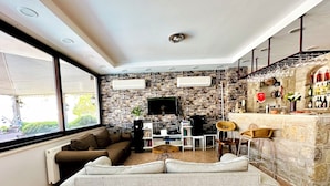 A modern living room with a sofa, a dining area, and a bar with wine bottles. - Villa Anfora Otel (Datça)