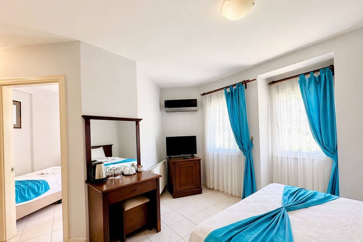 Una habitación de hotel con cama, escritorio con espejo, televisor y ventana con cortinas.