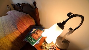 A neatly made bed with a colorful blanket, a bedside table with a book and a lamp, and a decorative pine cone. - Rifugio Del Parco (San Fratello)