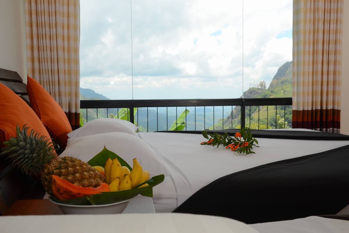 A hotel room with a bed, a fruit bowl, and a view of a mountainous landscape.