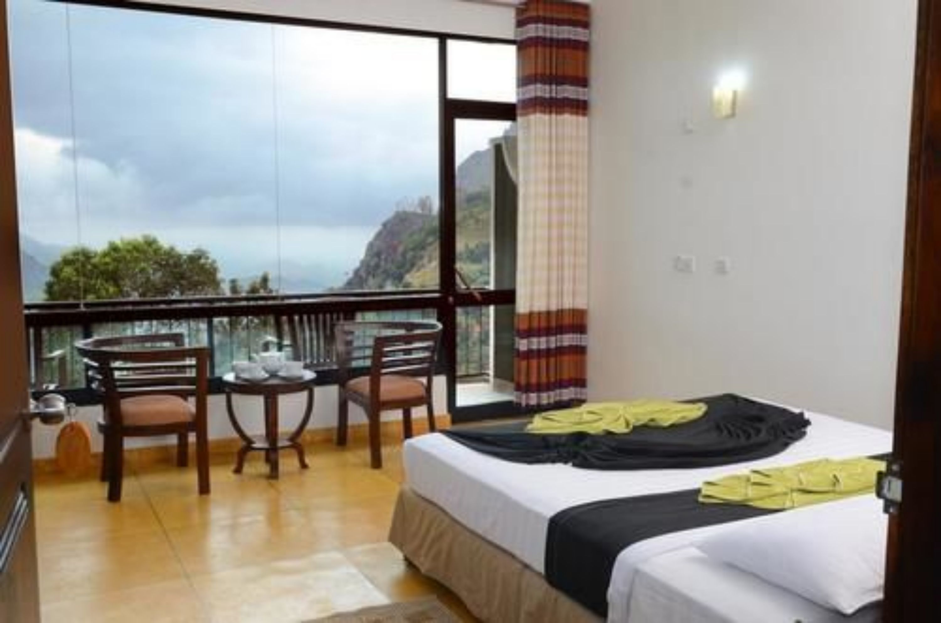Ein Hotelzimmer mit Balkon, einem Bett, einem Tisch mit Stühlen und Blick auf Meer und Berge.