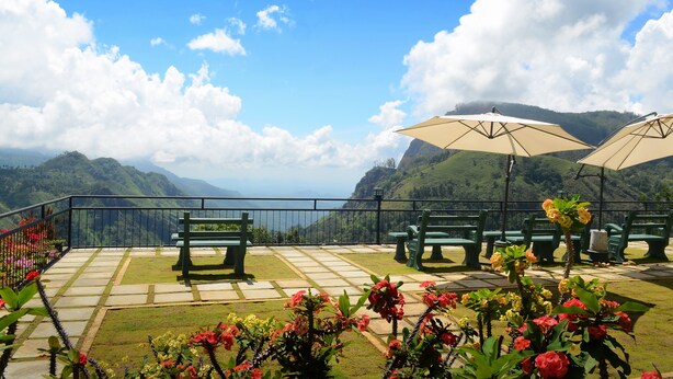 Une terrasse avec des bancs verts et des parasols beiges, offrant une vue sur un paysage montagneux.