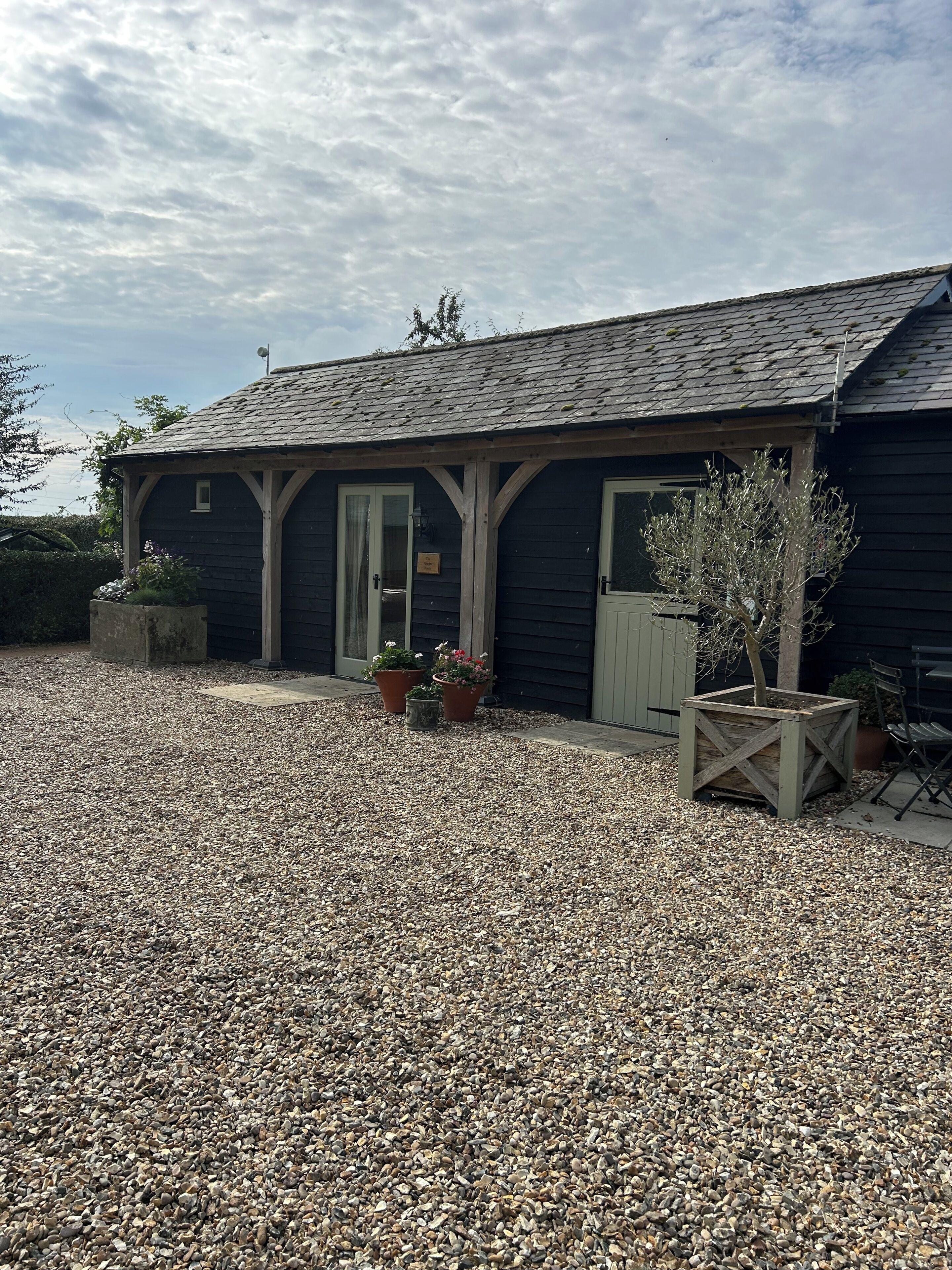 A building with a gravel driveway, wooden porch, and potted plants.