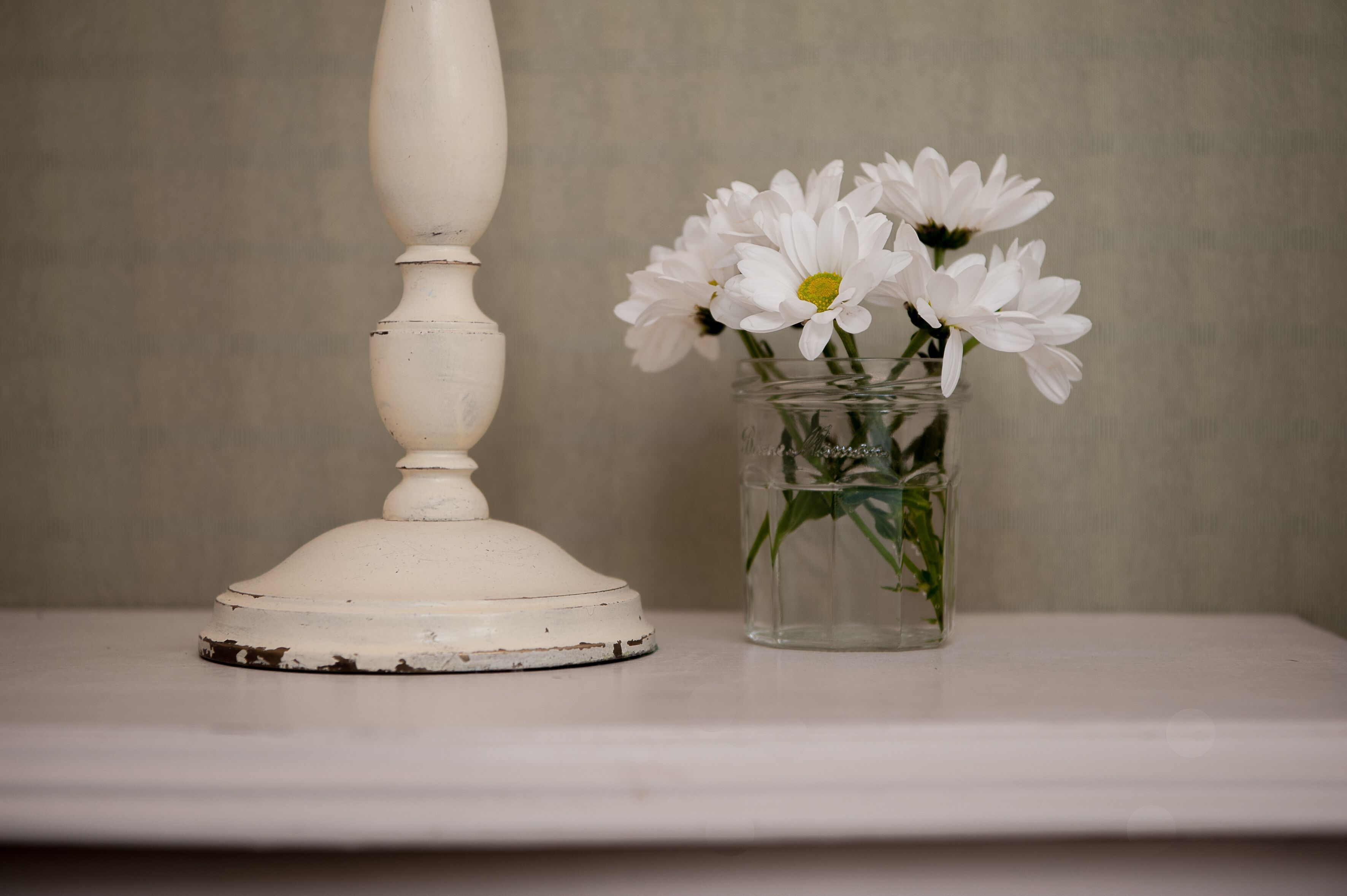 A white table with a vase of white flowers and a white candle holder.
