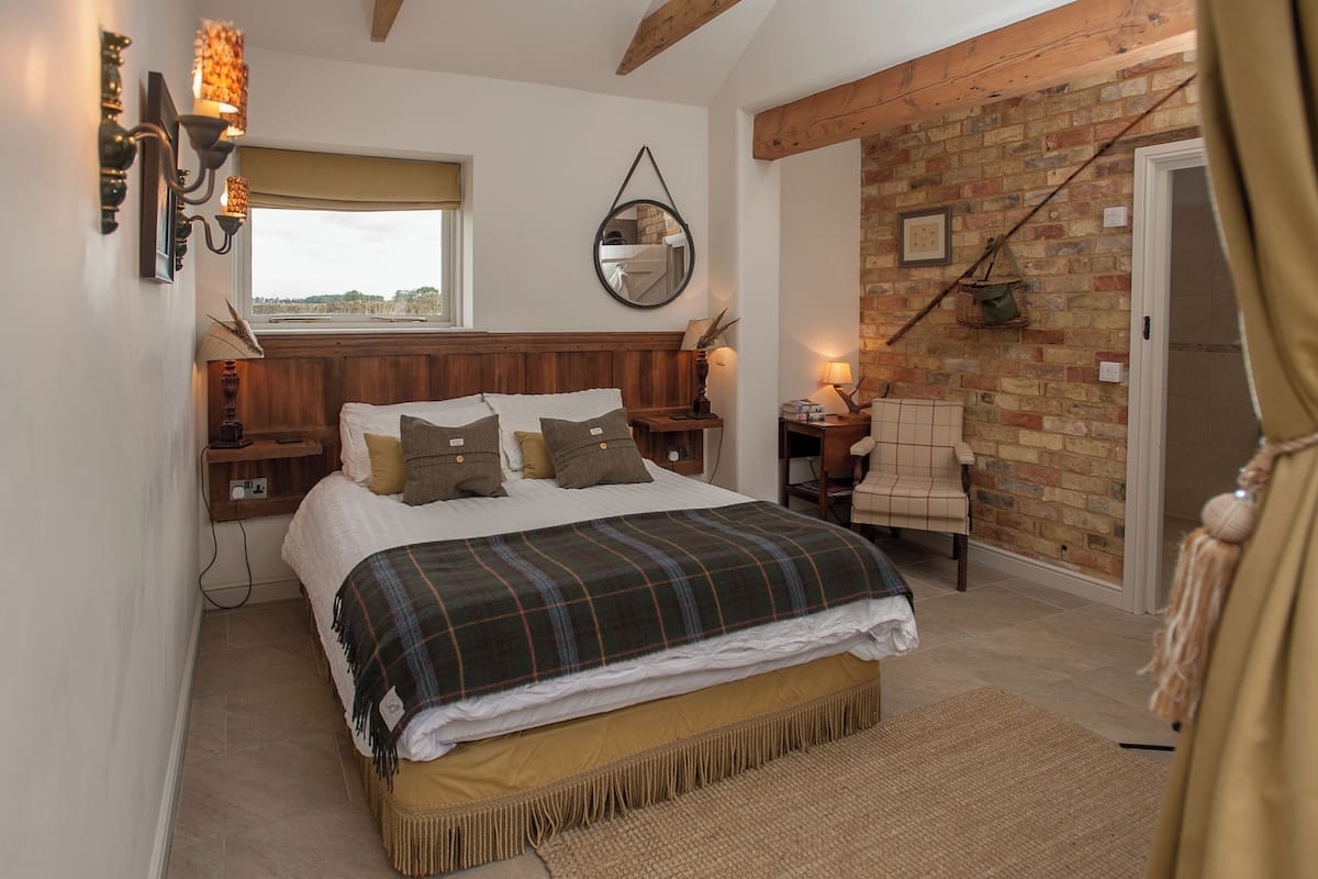 A cozy bedroom with a large bed, a wooden headboard, a brick wall, and a window with a view.