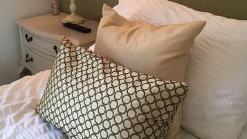 Un letto rifatto con cuscini fantasia e lisci, una lampada da comodino e un piccolo tavolino con un telecomando e un vaso di canne.