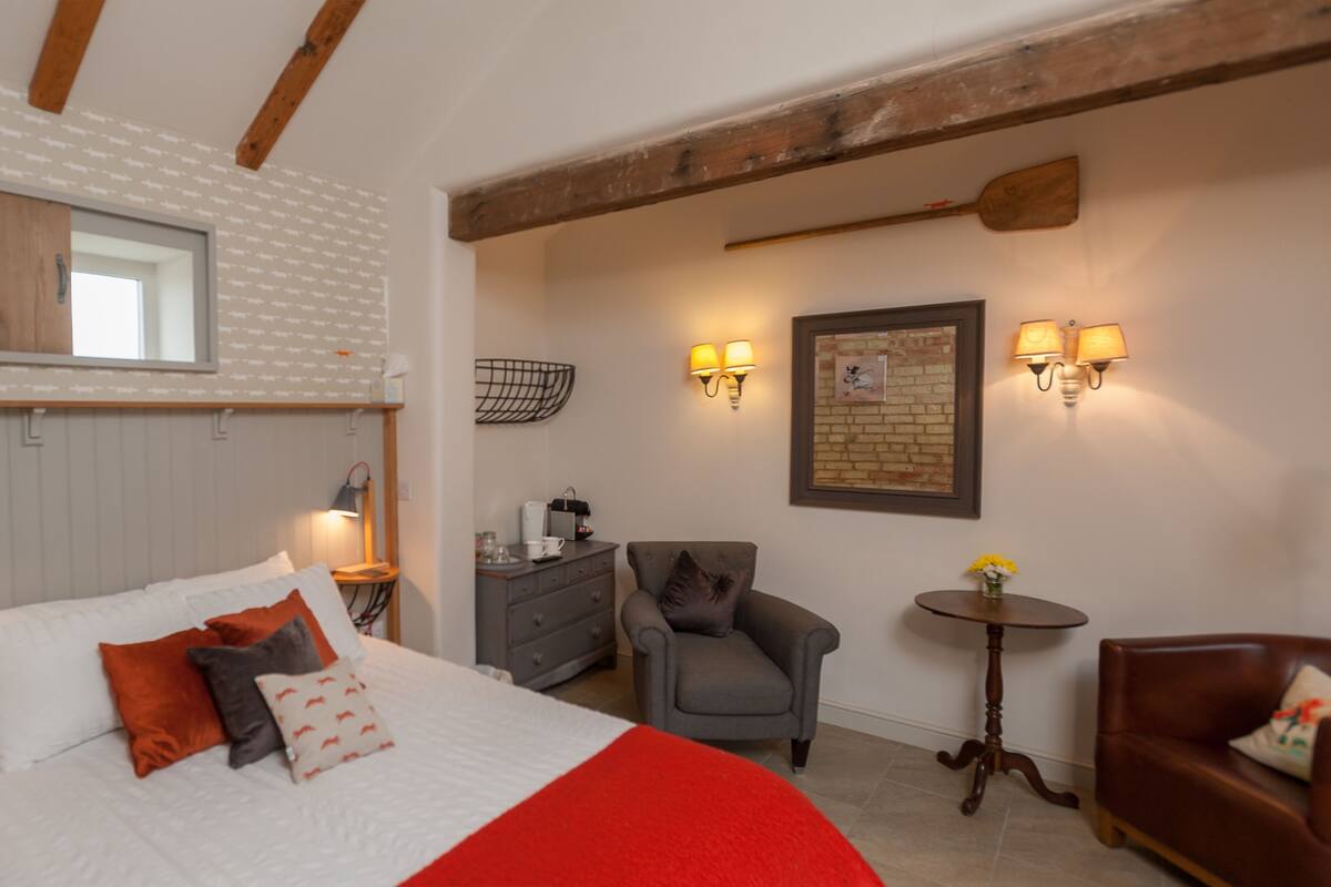 A bedroom with a bed, a chair, a small table, and a wall-mounted lamp.
