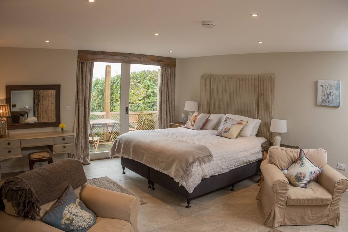 A bedroom with a large bed, a desk, a chair, and a balcony.