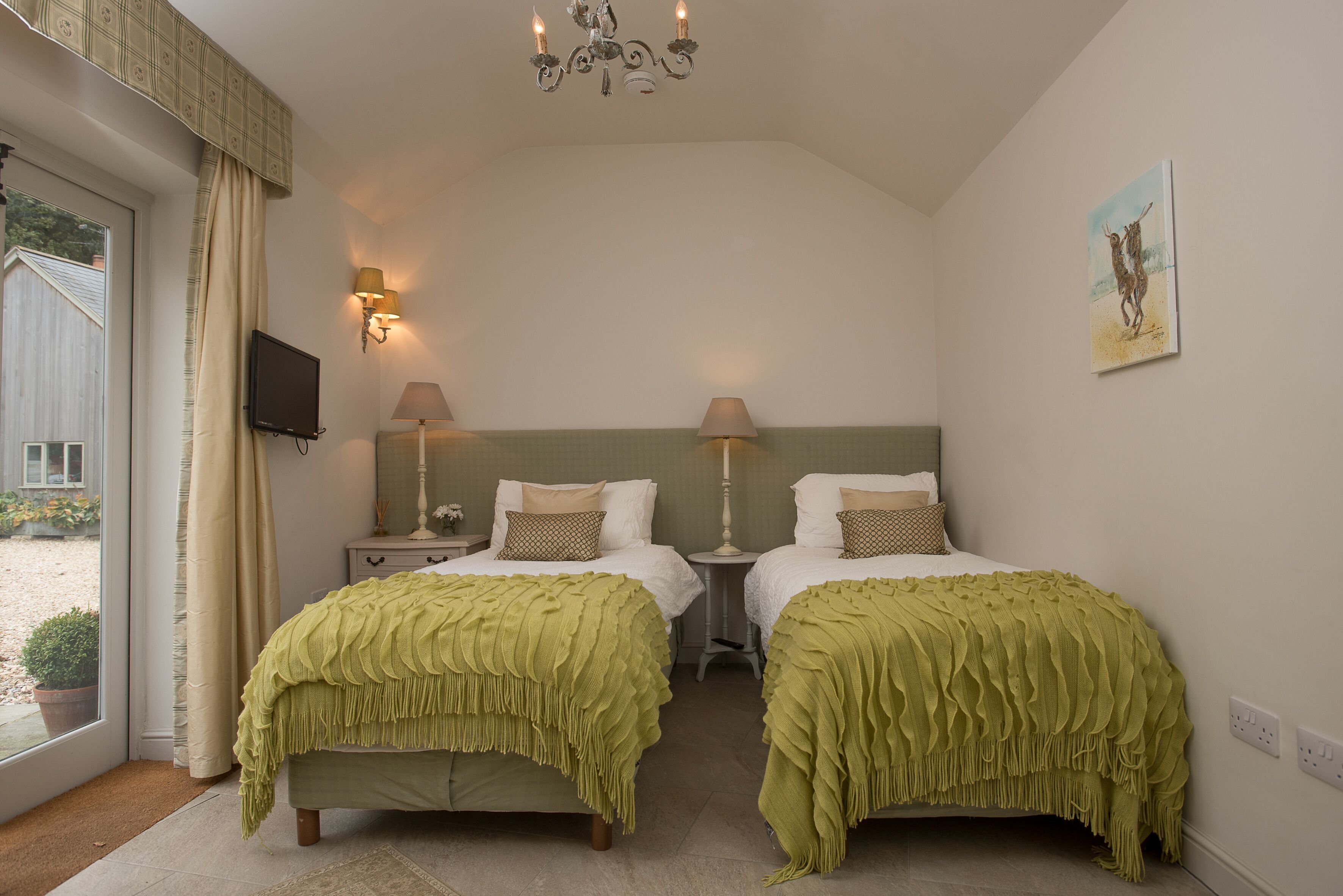 Ein Schlafzimmer mit zwei Betten, einer Kristallleuchtre, Wandlampen, einem Gemälde und einem Fernseher an der Wand.