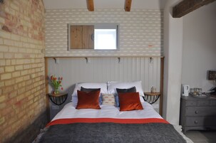 Un dormitorio con cama, mesita de noche, una pequeña mesa, una ventana y una pared de ladrillo.