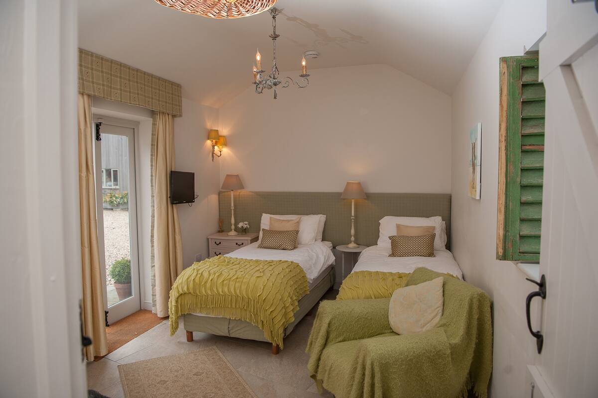 A bedroom with two beds, a chandelier, bedside lamps, a door with curtains, and a small potted plant.