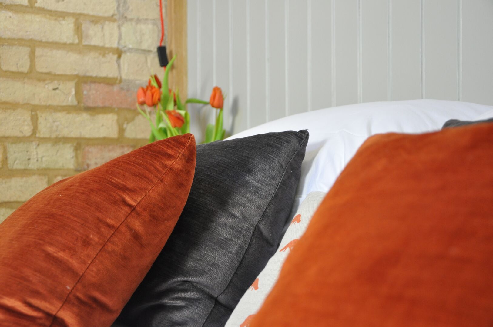 A bed with three pillows in different colors and a brick wall in the background.