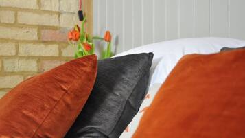A bed with three pillows in different colors and a brick wall in the background.