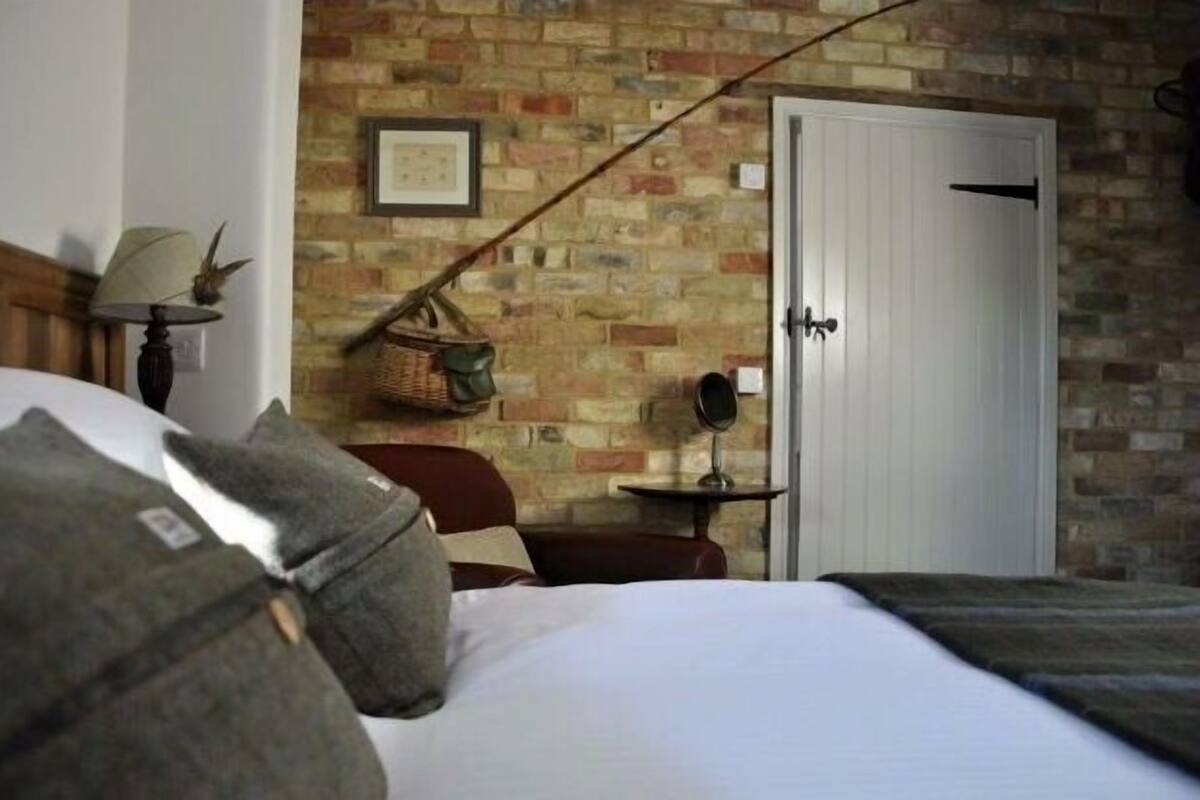 A bedroom with a brick wall, a white door, a bedside table with a lamp, and a hanging basket.