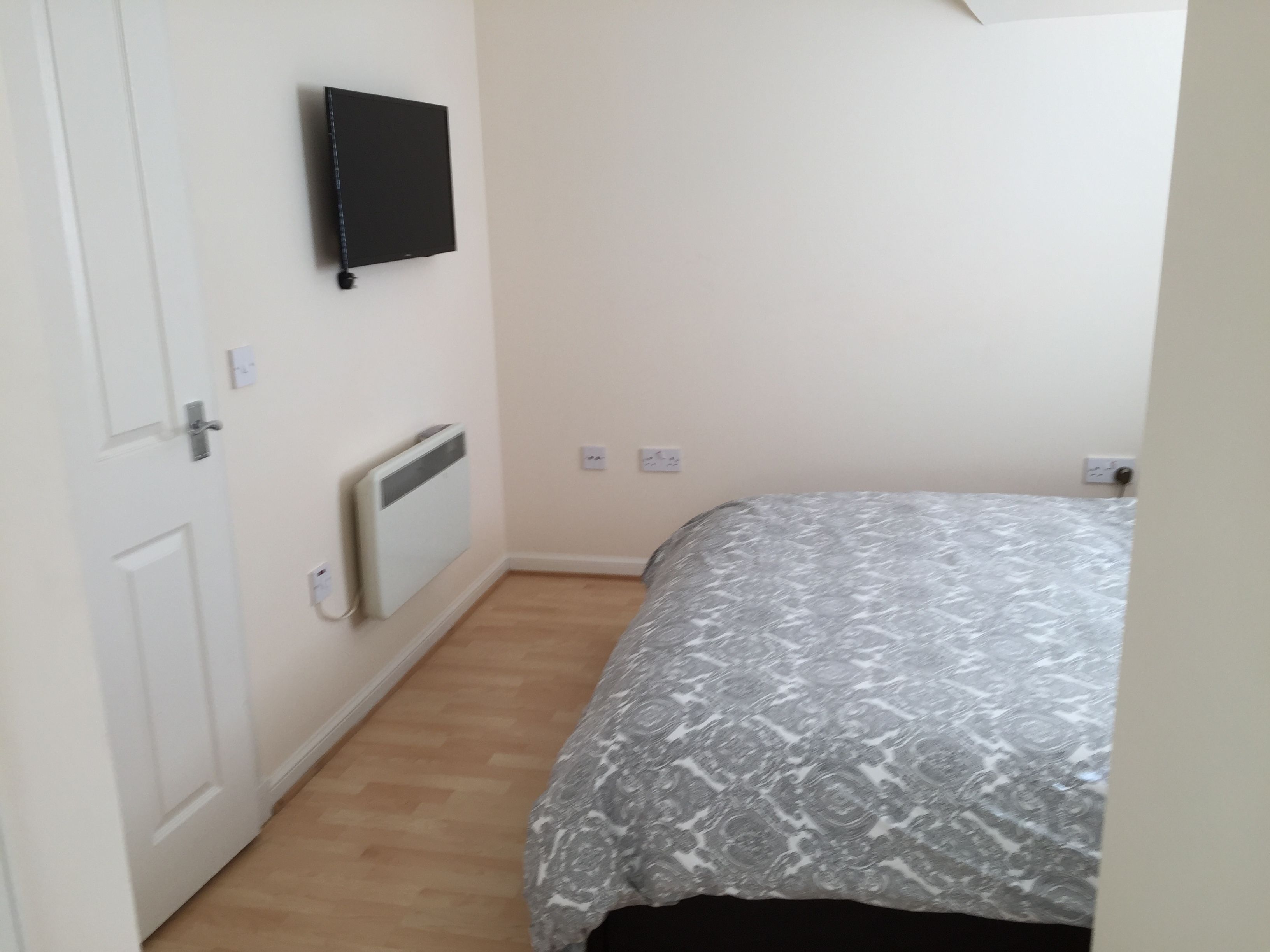 A bedroom with a bed, a radiator, a door, and a wall-mounted TV.