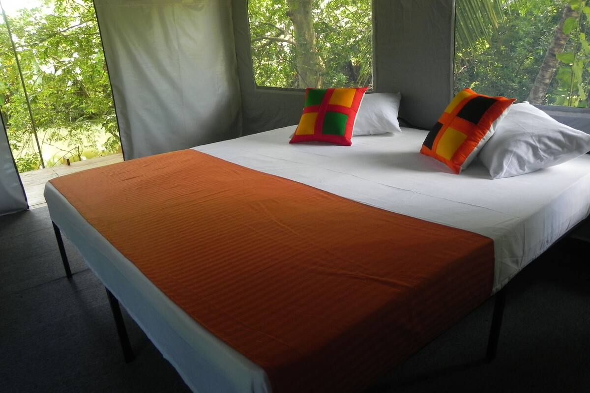 Un lit avec une couvre-lit orange, des oreillers blancs et des coussins décoratifs aux couleurs vives.
