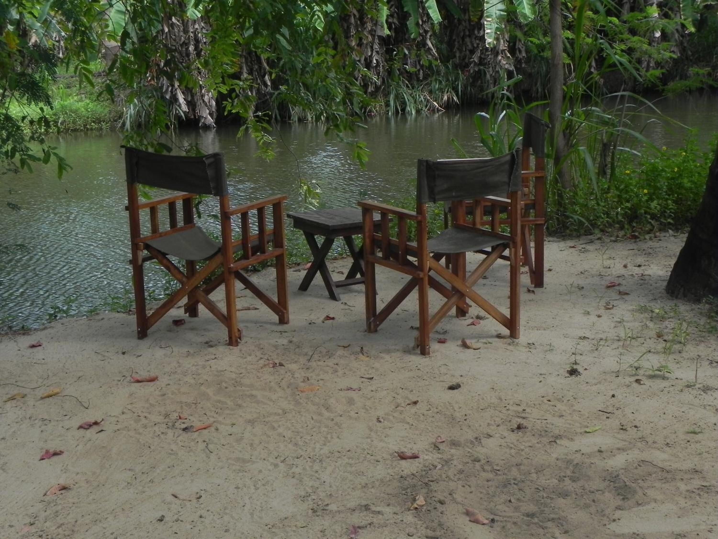 A sandy area with two wooden chairs and a small table near a body of water.