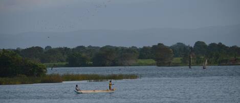 A calm lake with two canoes, one with a person paddling and another with a person standing.