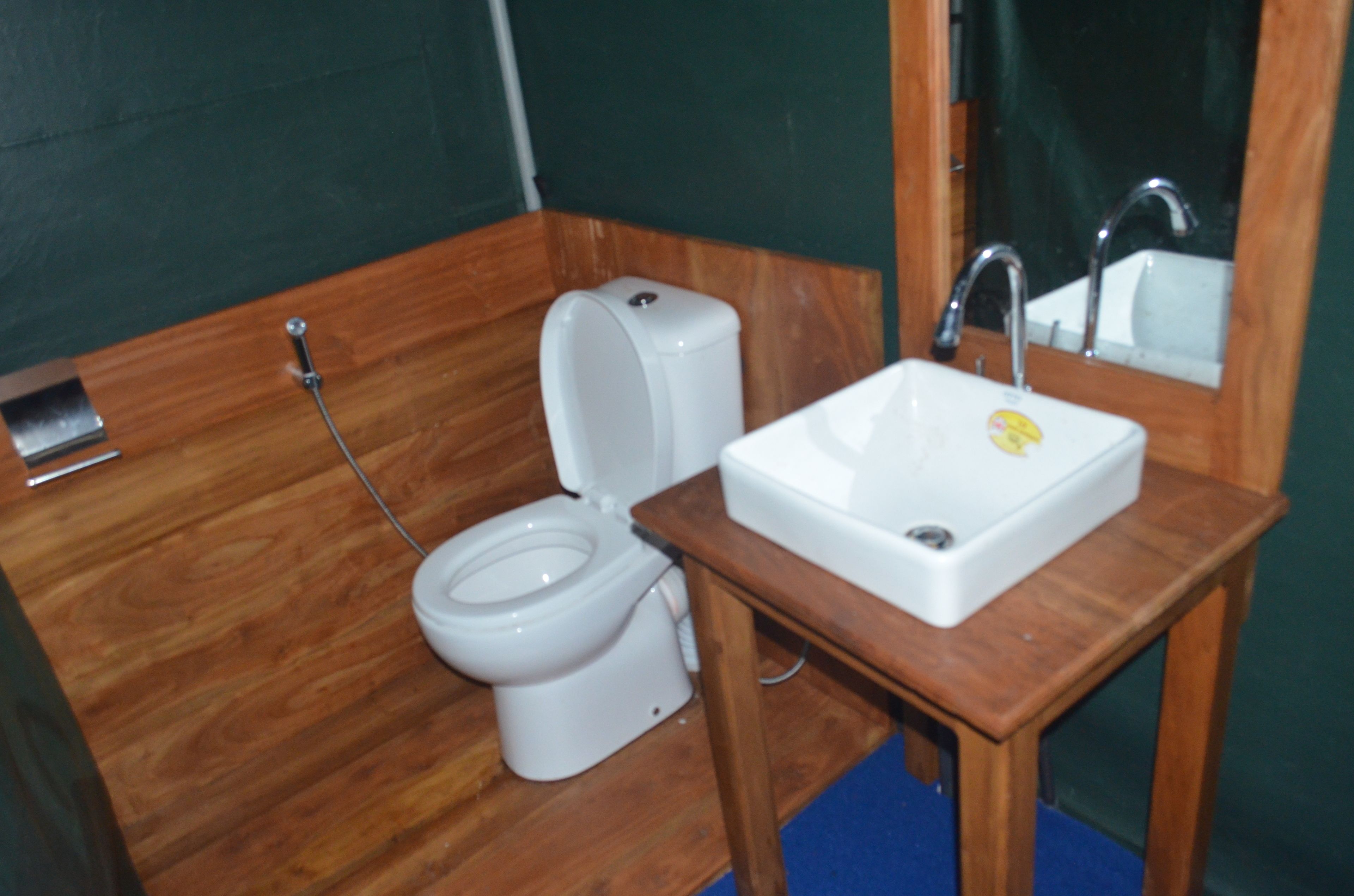 Une petite salle de bain avec un plancher en bois, des toilettes blanches, un lavabo blanc et un miroir au-dessus du lavabo.