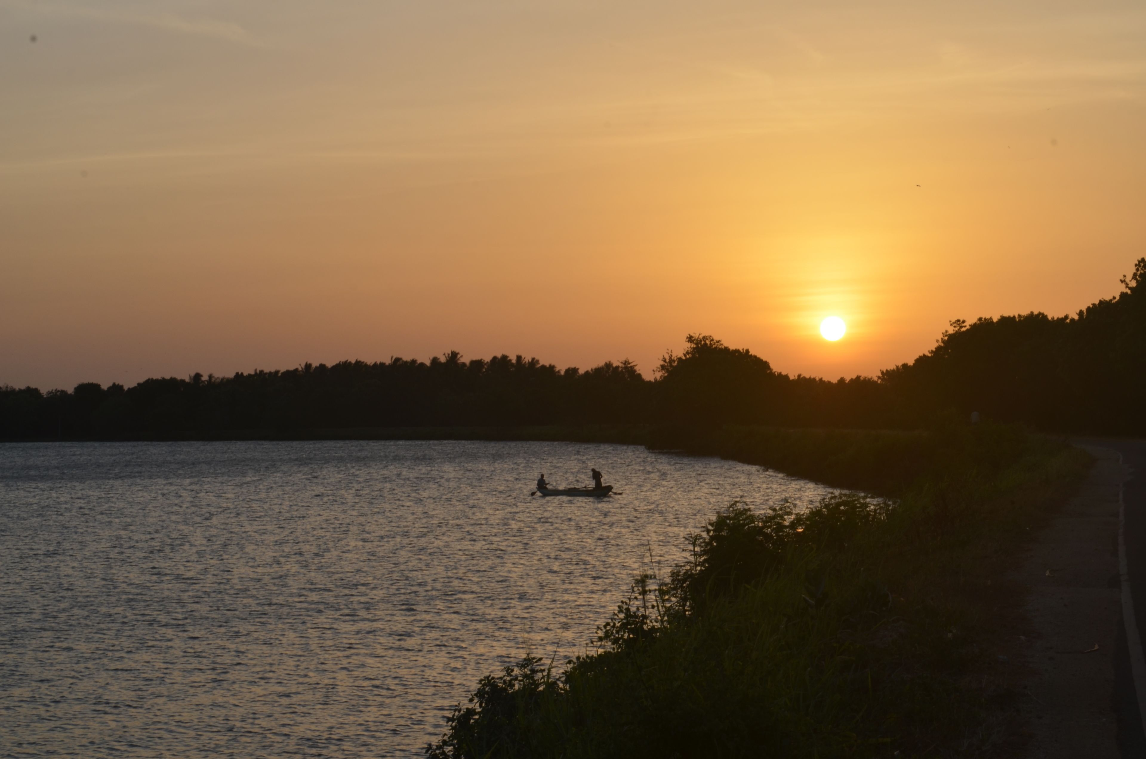 Un atardecer sobre un lago tranquilo con un bote y un camino a lo largo de la orilla.