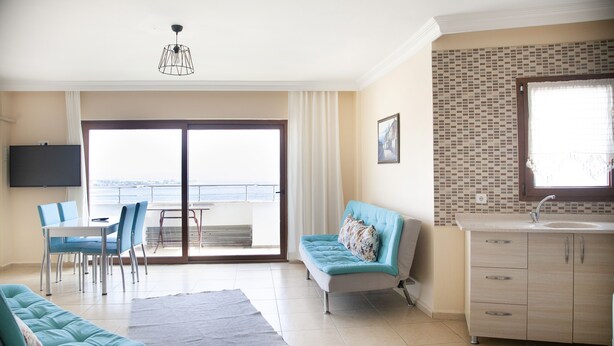 Uma sala de estar moderna com um sofá, uma mesa de jantar com cadeiras, uma televisão na parede e vista através de uma porta de vidro deslizante.