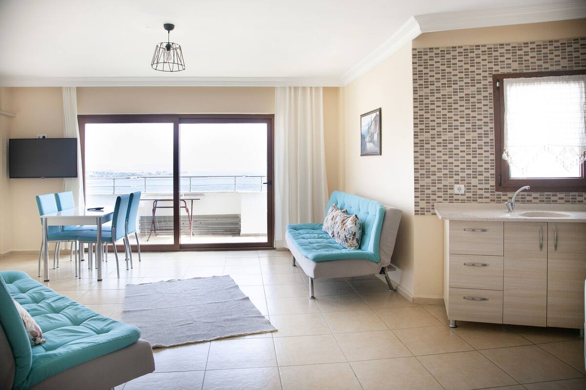 Una sala moderna con un sofá, una mesa de comedor con sillas, un televisor montado en la pared y vistas a través de una puerta corrediza de vidrio.