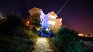 Um caminho de pedras leva a um edifício com várias andares, varandas iluminadas e céu noturno.