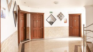 Um corredor com três portas de madeira, um espelho em formato de losango e uma escadaria.