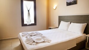Quarto de hotel com cama, janela com cortina, mesa de cabeceira e luminária na parede.