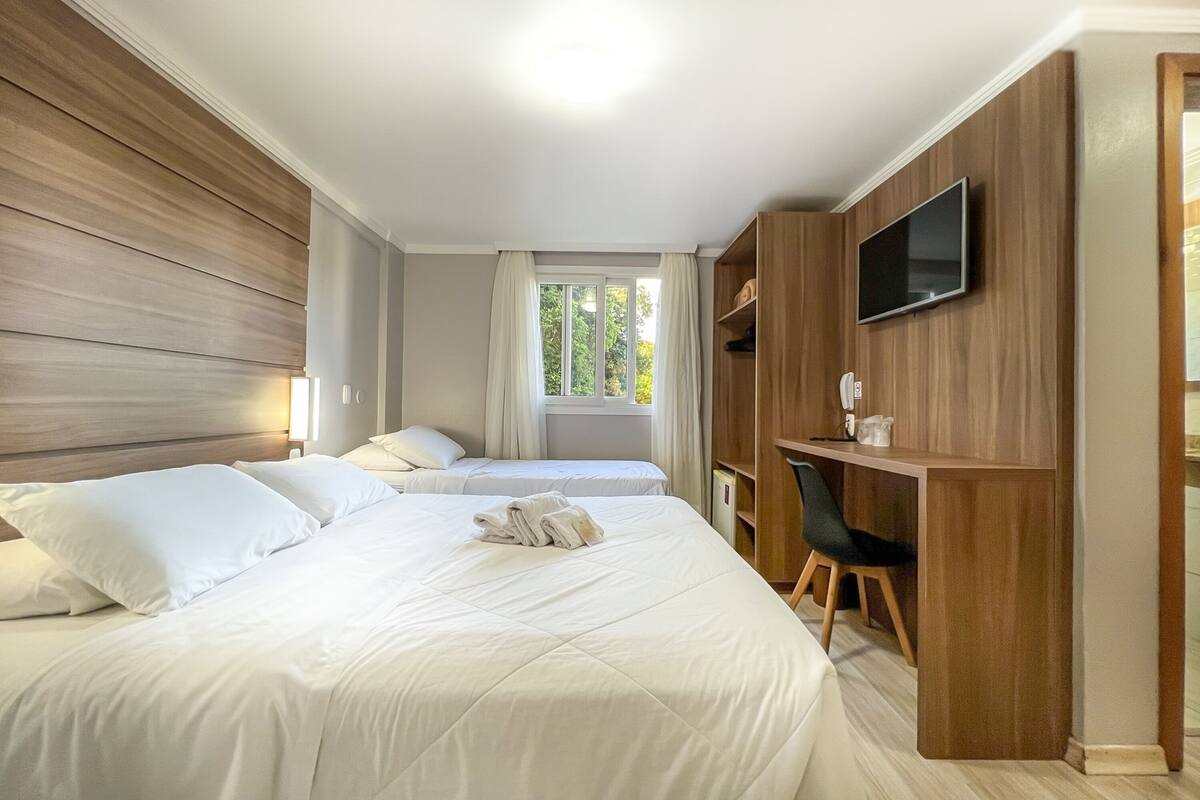 Une chambre d’hôtel avec deux lits, un bureau, une chaise, une télévision et une fenêtre avec des rideaux.