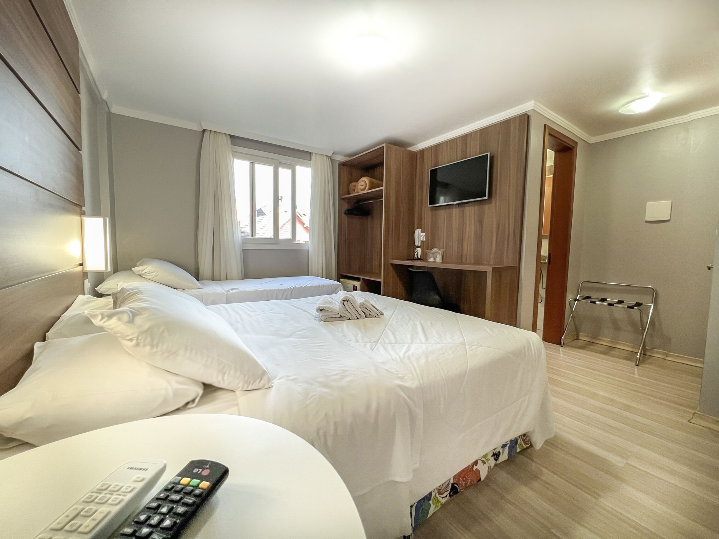 Camera d'albergo con due letti, una televisione, una scrivania con una sedia e un piccolo tavolino con un telecomando.