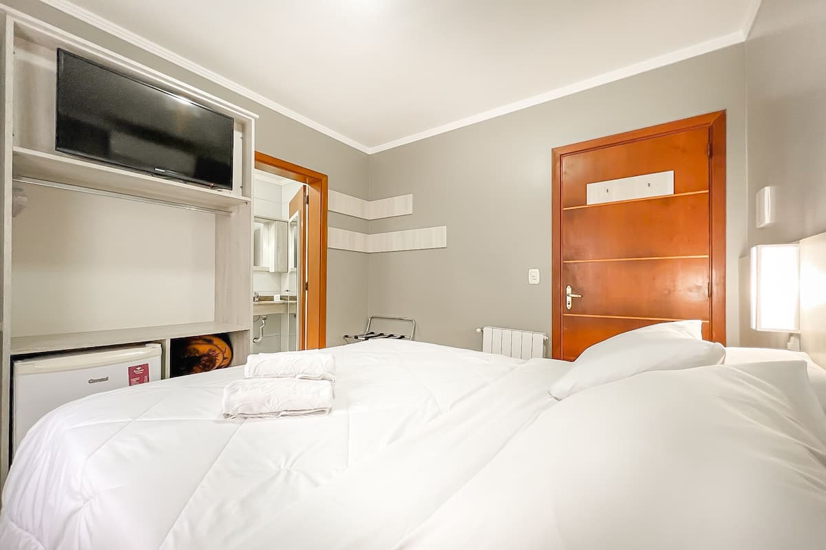 Une chambre d’hôtel avec un grand lit, une armoire, un miroir et une télévision.