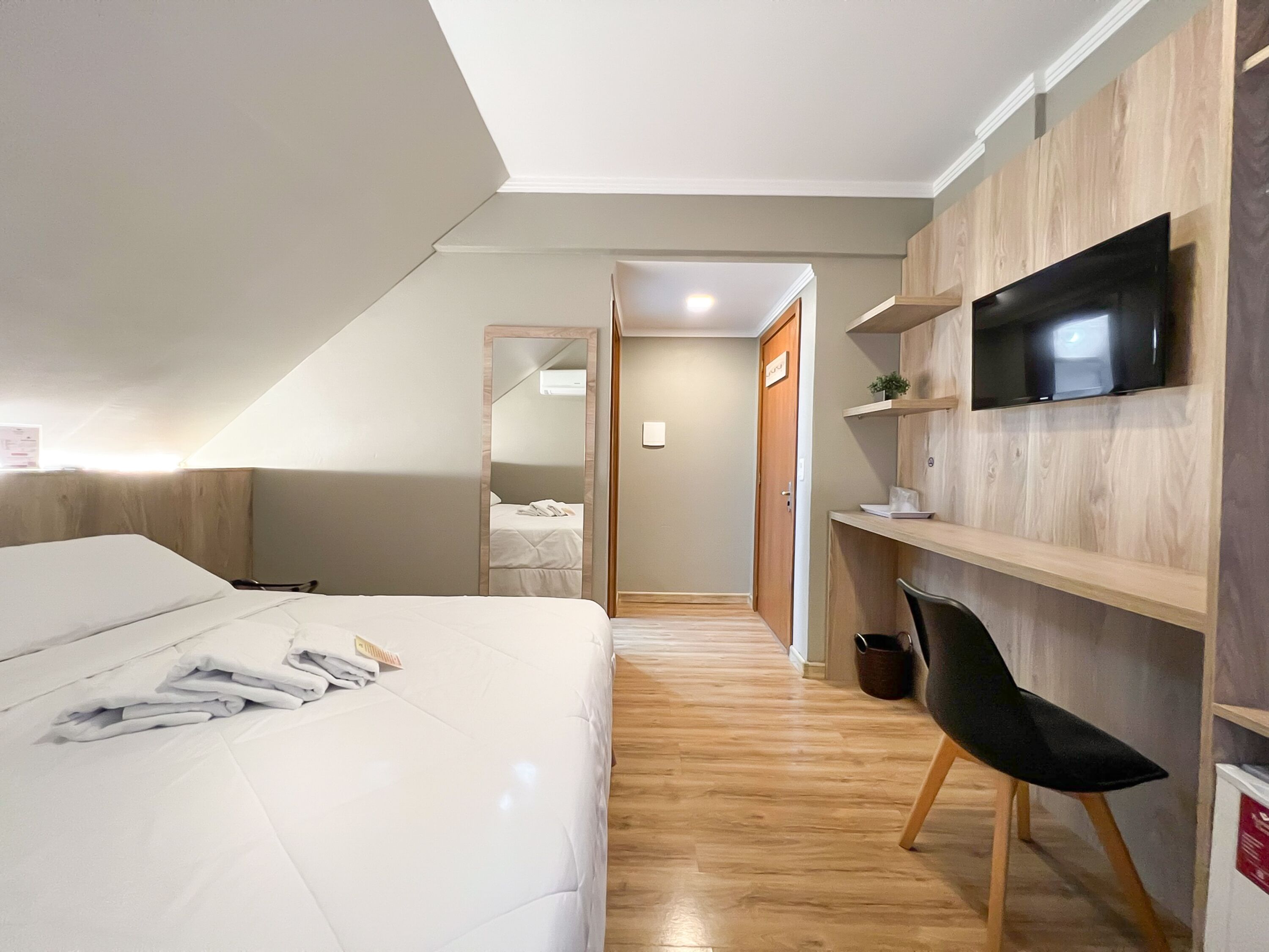 A bedroom with a bed, a desk, a TV, and a mirror.