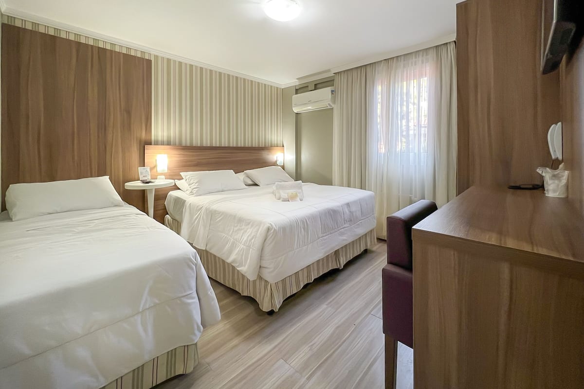 Une chambre d’hôtel avec deux lits, un bureau, une chaise, une télévision et une fenêtre avec des rideaux.