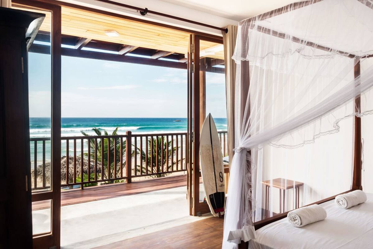 A bedroom with a bed, a surfboard, and a view of the ocean.