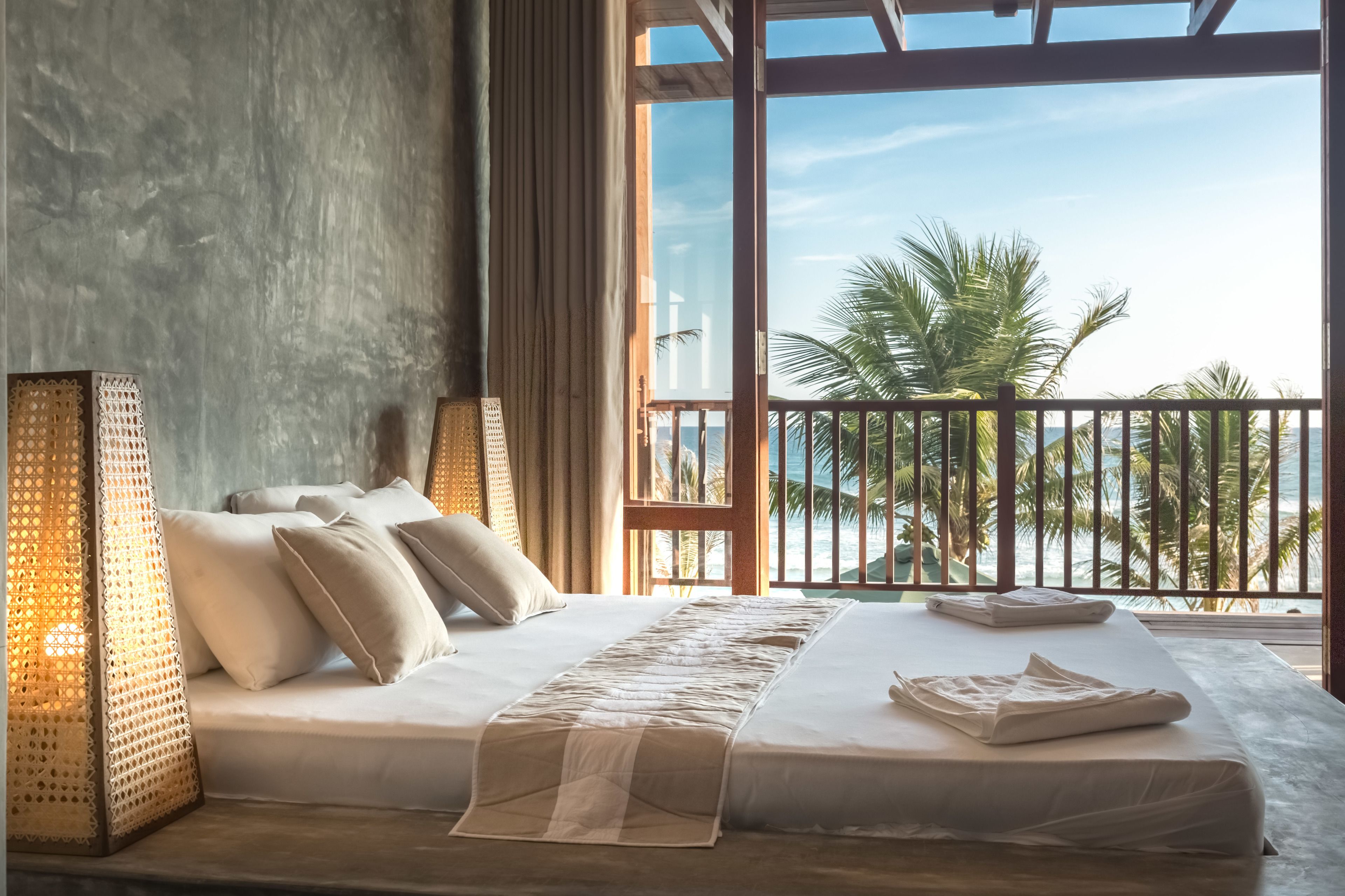 Une chambre avec un grand lit, une vue sur les palmiers et l’océan, et un balcon doté d’une balustrade.