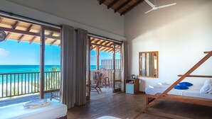 Une chambre d’hôtel avec un balcon donnant sur l’océan, un ventilateur de plafond et un lit avec des oreillers.