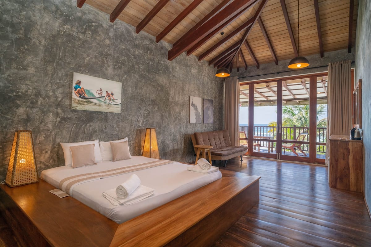 A spacious bedroom with a large bed, wooden headboard, and a view of the outdoors through a glass door.