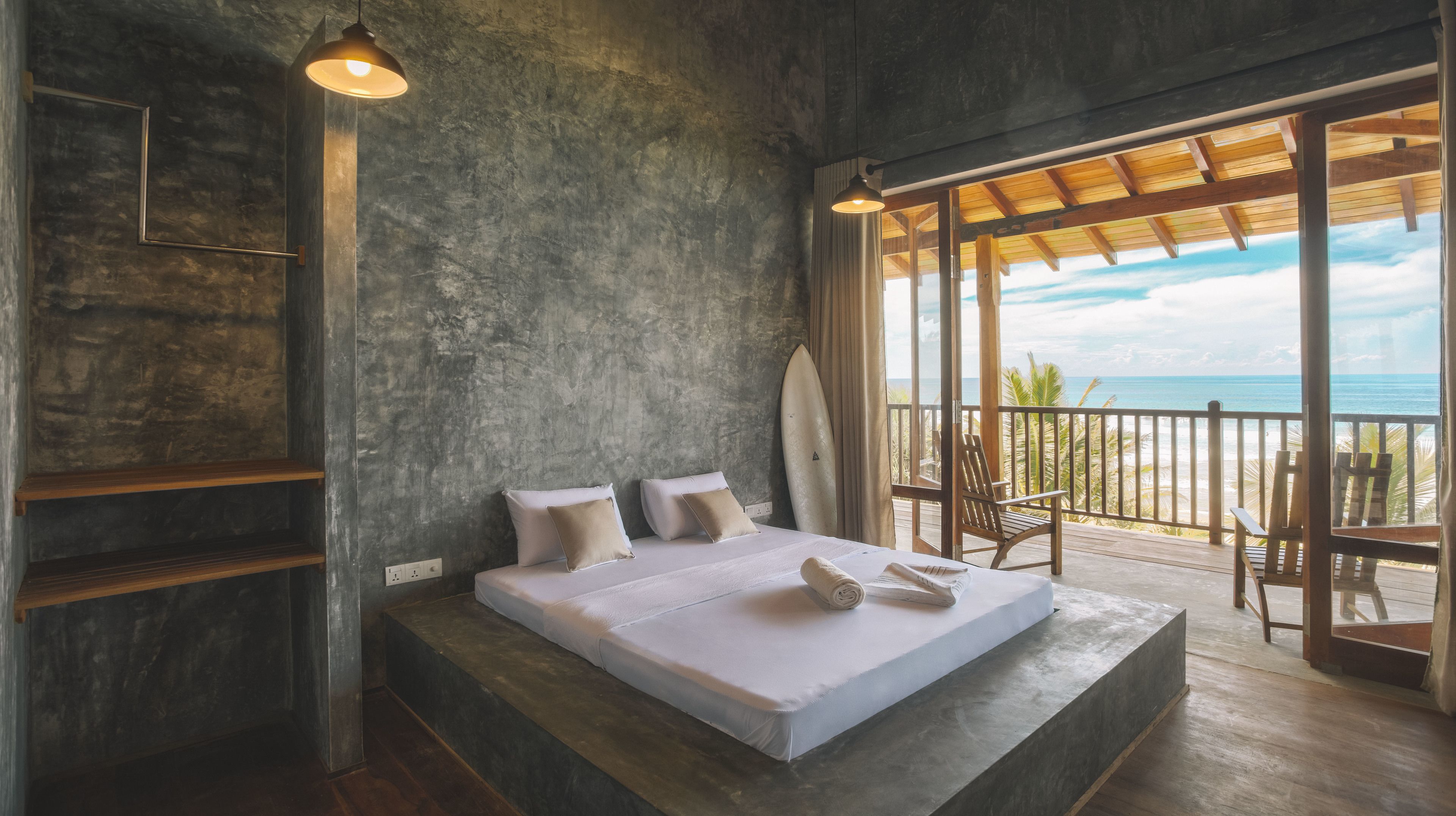 A bedroom with a large bed, a surfboard, and a view of the beach.