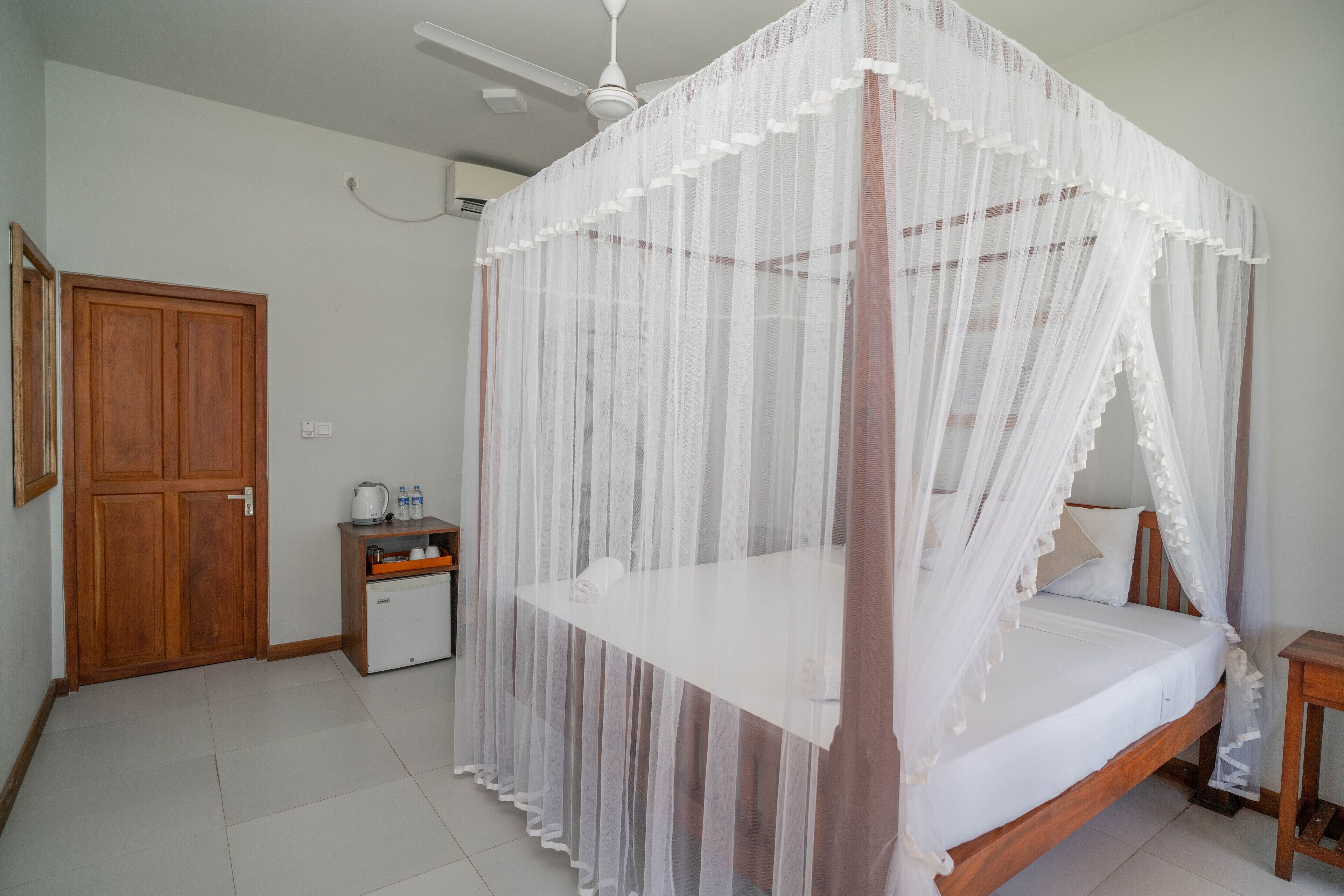 Um quarto com cama de dossel, guarda-roupa de madeira, uma pequena mesa de cabeceira e um criado-mudo.