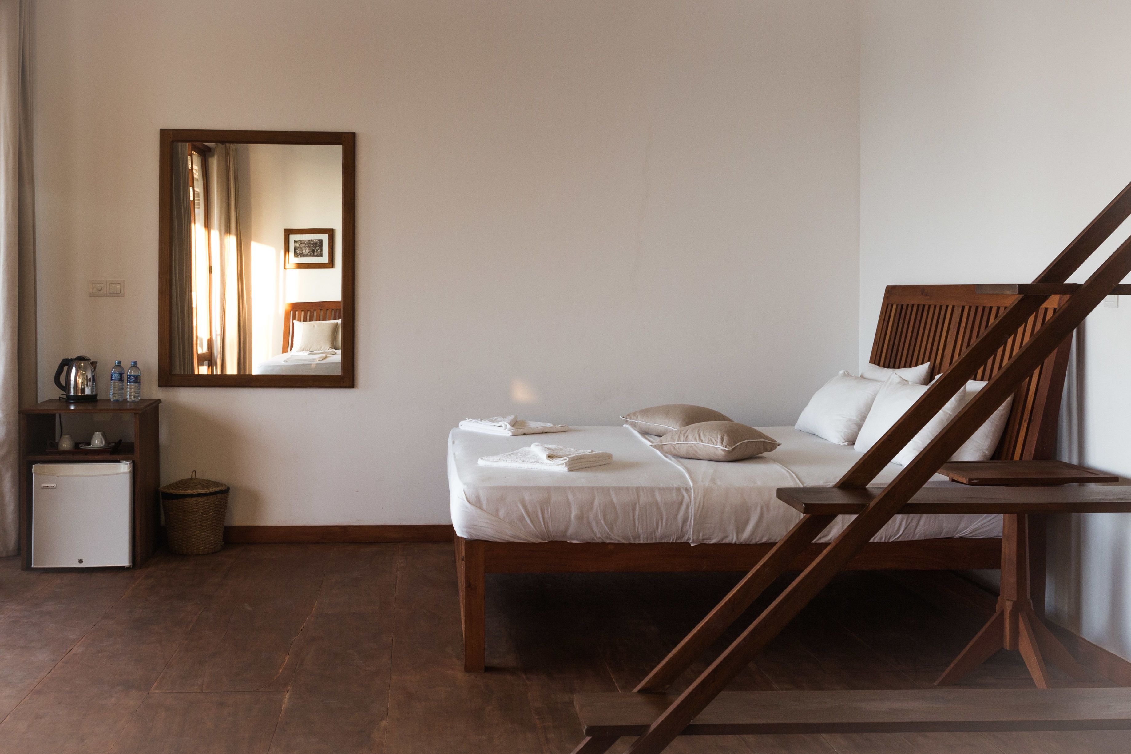 A bedroom with a wooden bed, a small bedside table, a mirror, and a white wardrobe.
